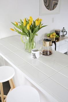 a kitchen counter with yellow flowers in a vase and two cups on the counter top