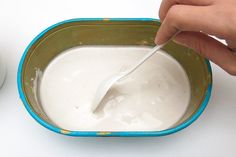 a person is spooning milk into a blue and green bowl on a white surface