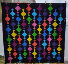 a black quilt with multicolored diamonds on it hanging from a clothes line in front of a house