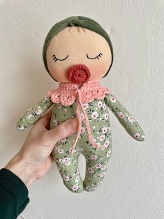 a hand holding a small doll with a pink nose and green floral print on it