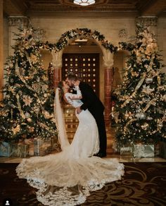 a bride and groom kissing in front of christmas trees