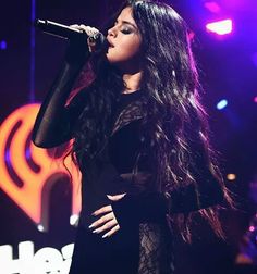 a woman with long black hair on stage holding a microphone and singing into the air