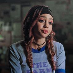 a woman with long braids wearing a blue shirt and black headband looking at the camera