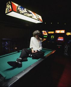 a man sitting on top of a pool table in front of a neon light sign