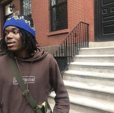 a young man with dreadlocks and a blue hat standing in front of stairs