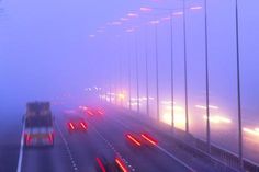 cars driving on a foggy highway in the middle of the night with lights from headlights