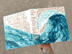 a person holding up a book with an ocean painting on it