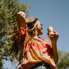 a woman with her hair blowing in the wind and holding a can of soda up to her face