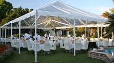 a group of people sitting at tables under a white tent next to a swimming pool