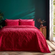 a bedroom with green walls and red bedspread on the bed in front of an open window