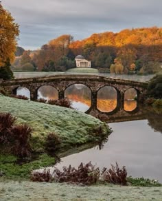 an old stone bridge over a small pond in the middle of a field with trees and grass around it