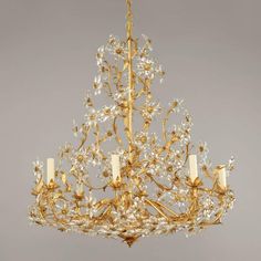 a gold chandelier with white candles and flowers on the bottom, hanging from a ceiling