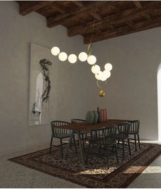 a dining room table with chairs and lights hanging from it's ceiling, in front of a painting on the wall