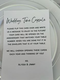 a table setting with a white plate and wedding card on top of it, which is written in cursive writing