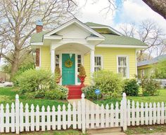 a small yellow house with a green door and white picket fence in front of it