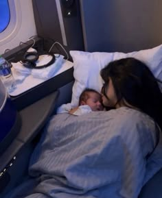 a woman holding a baby in bed next to an air plane window with the lights on