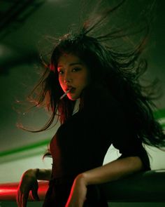 a woman with long hair standing in front of a red light and looking at the camera