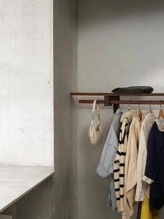 a rack with clothes hanging on it next to a white wall and shelf in the corner