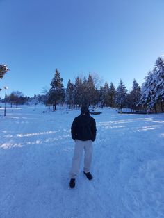 a person standing in the snow with their back turned to the camera and trees behind them