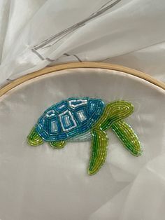 a close up of a small embroidered turtle on a piece of white fabric with a wooden hoop