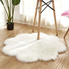 a white sheepskin rug is on the floor next to a pink chair and potted plant