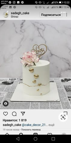 a white cake with gold decorations and flowers on top, sitting on a table in front of a marble background