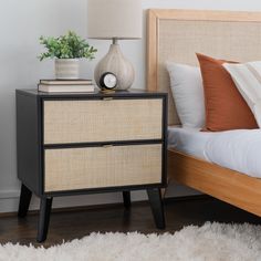 a nightstand with two drawers and a clock on it next to a white bed in a bedroom