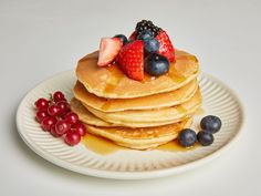 a stack of pancakes topped with fruit on top of a white plate next to berries and syrup