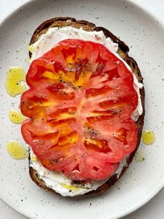 a white plate topped with a piece of bread covered in cheese and tomato slices on top of it