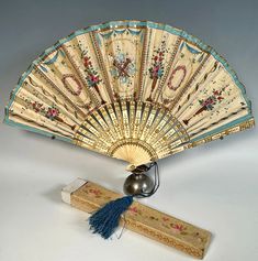 an antique hand fan with blue tassels sits next to a piece of wood