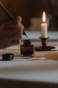 a person writing on a piece of paper next to a lit candle and ink bottle