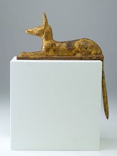 a golden dog figurine sitting on top of a white block in front of a gray background