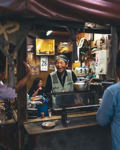 a man standing in front of a counter with people sitting at it and talking to each other