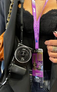 a woman wearing a black bra and holding a camera in her hand with a purple lanyard around her neck