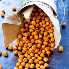 roasted chickpeas spilling out of a tin can onto a blue surface with paper bag