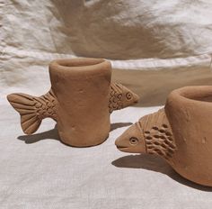 two clay fish shaped vases sitting on top of a white cloth covered tablecloth