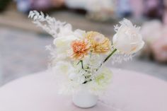 a white vase filled with flowers sitting on top of a pink tablecloth covered table