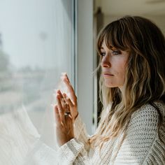 a woman is looking out the window and holding her hands together