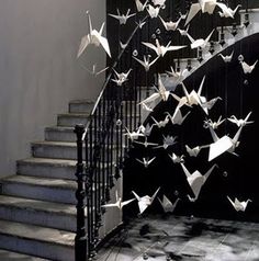 there are many origami birds flying down the stairs in this house that is decorated with wrought iron railings