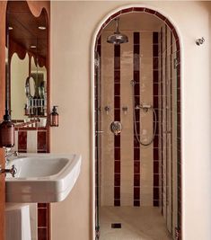 a white sink sitting under a bathroom mirror next to a walk in shower with an arched doorway