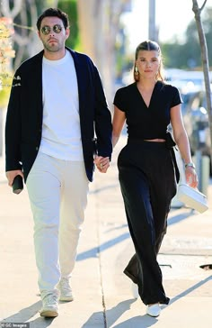 a man and woman walking down the street holding hands while wearing black outfits with white shoes