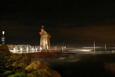 the lighthouse is lit up at night by the water