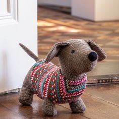 a stuffed dog is wearing a sweater and standing on the floor next to a door