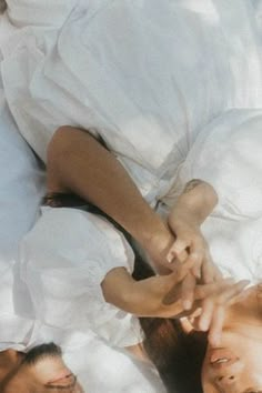 two people laying in bed with white sheets