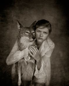 a woman is holding a wolf in her arms and posing for a photo with it's eyes open