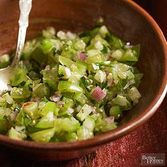 a brown bowl filled with chopped green vegetables and a spoon in it's side