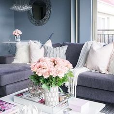 a living room filled with furniture and flowers on top of a coffee table in front of a window