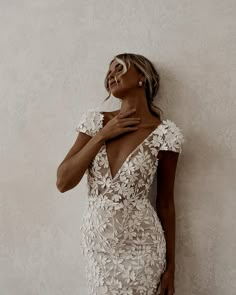 a woman in a white dress leaning against a wall with her hand on her chest