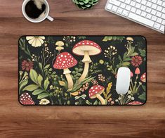 a mouse pad with mushrooms and flowers on it next to a keyboard, coffee cup and plant