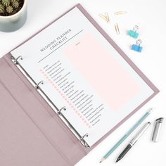 a pink binder next to a pen and some office supplies on a white table